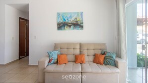 A living room with a beige sofa, two orange cushions, and a colorful painting of boats on the wall. - Apt w/ Barbecue 500m From the Beach Pbr1003 (Porto Seguro)