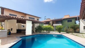A swimming pool with tiled edges, surrounded by a covered patio area, and adjacent buildings with tiled roofs. - Apt w/ Barbecue 500m From the Beach Pbr1003 (Porto Seguro)