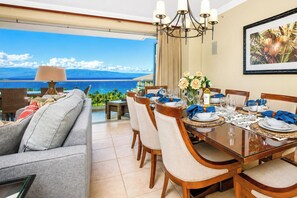 A dining area with a view of the sea, a chandelier, and a table set for a meal.