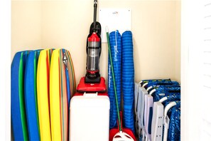 Una habitación con una aspiradora, tablas de surf coloridas y una maleta blanca.
