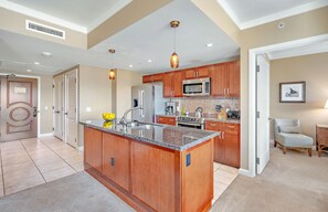 Une cuisine moderne avec des meubles en bois, un plan de travail en granit, des appareils électroménagers en acier inoxydable et des luminaires suspendus.
