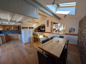 Una cocina amplia con armarios de madera, un comedor con mesa y sillas de madera, y un tragaluz arriba.