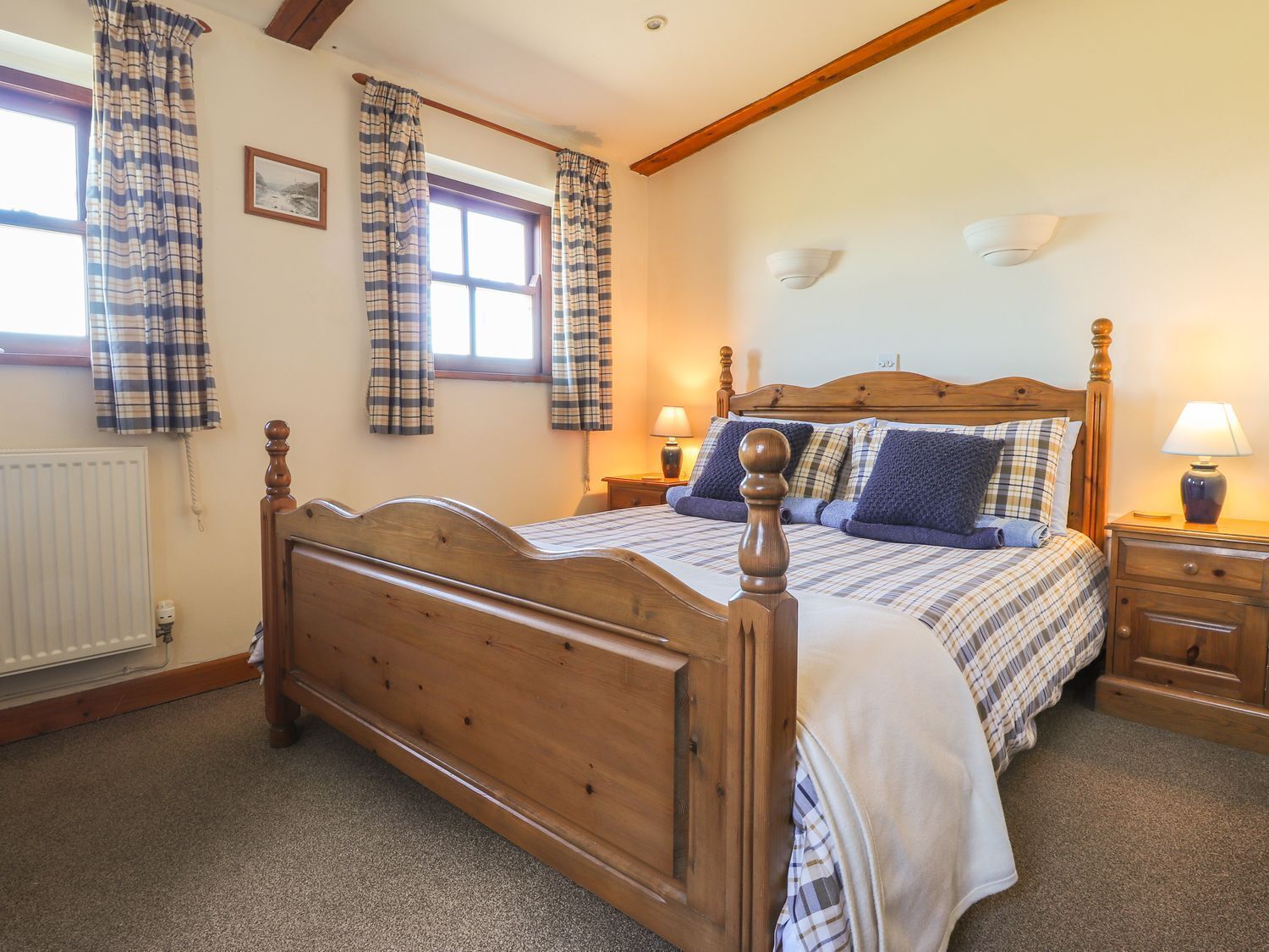 A bedroom with a wooden four-poster bed, plaid curtains, a window with a view, and a bedside table with a lamp.