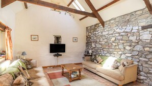 Una sala de estar acogedora con pared de piedra, vigas de madera, un televisor de pantalla plana y un sofá cómodo.