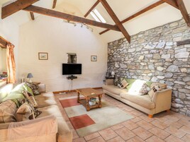 Una sala de estar acogedora con pared de piedra, vigas de madera, un televisor de pantalla plana y un sofá cómodo.