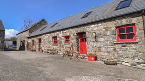 Edificio de piedra con ventanas y puertas rojas, un techo inclinado y una pequeña estructura adosada con un ventanal.