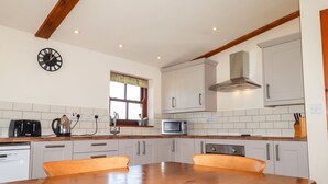 Una cocina con armarios blancos, una mesa de madera, un tostador, un hervidor, un microondas y un reloj en la pared.