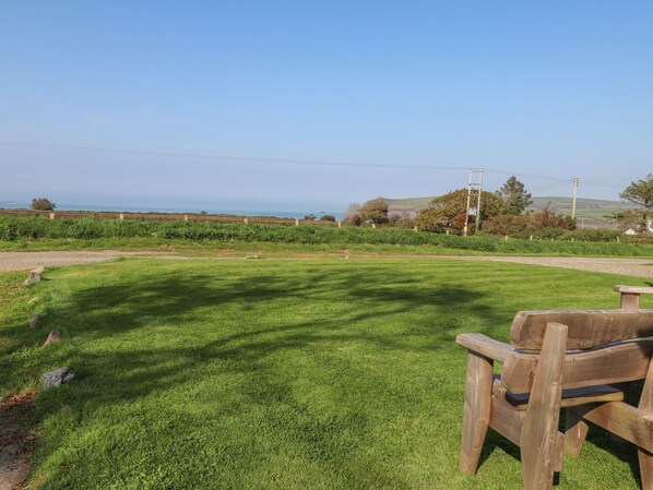 A grassy field with a wooden bench and a view of the sea. - Ty Cariad (Newport)