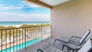 A balcony with two lounge chairs, a pool, and a view of the beach and ocean. - Beachfront condo with washer dryer pool and hot tub dog friendly (Indian Rocks Beach)