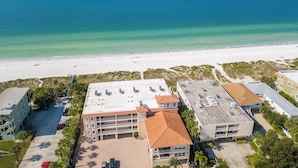An aerial view of a coastal hotel with multiple buildings, a parking lot, and a beach in the background. - Beachfront condo with washer dryer pool and hot tub dog friendly (Indian Rocks Beach)
