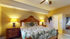 A bedroom with a wooden bed, two bedside tables with lamps, a ceiling fan, and a door leading to another room. - Welcoming Gulf front condo with pool and hot tub direct beach access (Indian Rocks Beach)