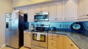 A kitchen with stainless steel appliances, white cabinets, and a patterned backsplash. - Welcoming Gulf front condo with pool and hot tub direct beach access (Indian Rocks Beach)