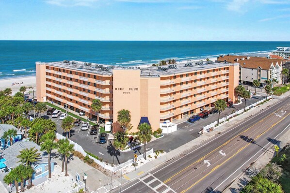 A large hotel with multiple floors, a prominent sign reading 'REEF CLUB 1000', and a view of the beach and ocean. - Bright and recently redone condo hot tub pool and tennis direct beach access (Indian Rocks Beach)