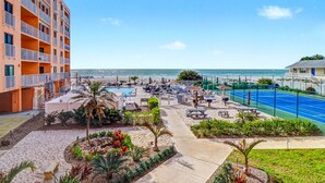 Ein Hotel direkt am Strand mit Pool, Tennisplatz und mehreren Balkonen.