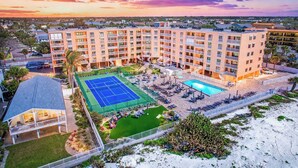 Ein mehrstöckiges Hotel mit Tennisplatz, Pool und Außenbereich mit Sitzgelegenheiten.