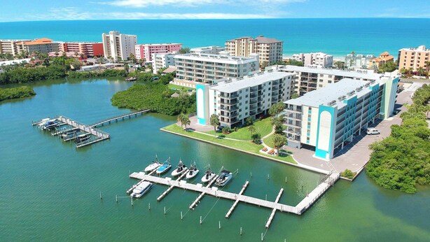 Un puerto deportivo con barcos amarrados, un edificio grande de varios pisos y vista al océano.