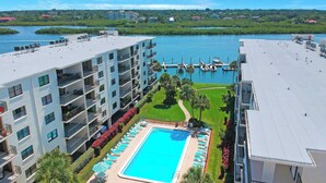 Un hotel con piscina en la azotea, varios balcones y vistas a un puerto deportivo.