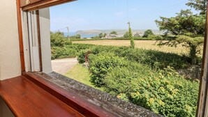 A window view of a rural landscape with fields, trees, and a distant coastline. - Ty Fferm (Newport)