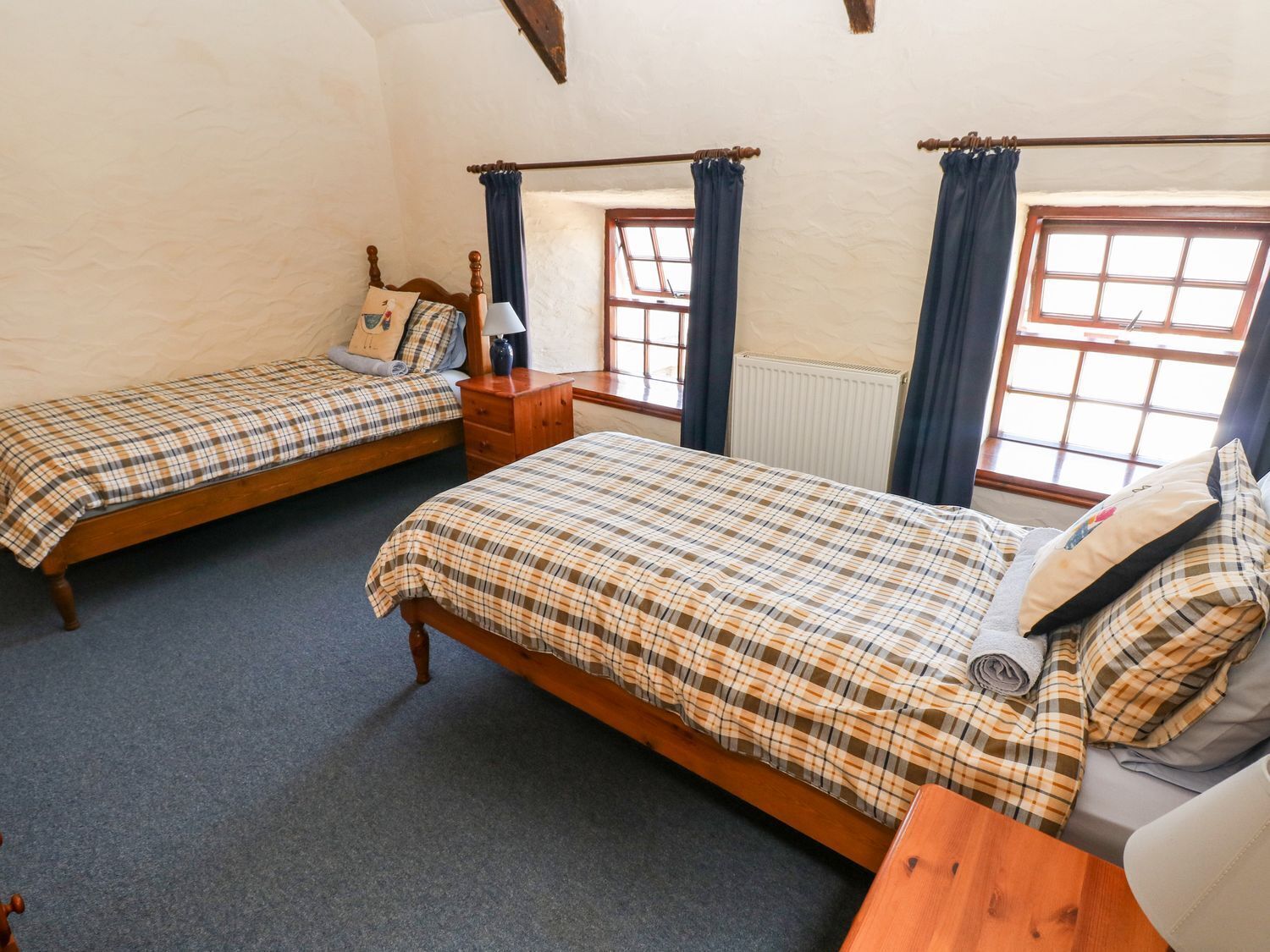 Una habitación con dos camas individuales, una mesita de noche de madera, una pequeña mesa y una ventana con cortinas.