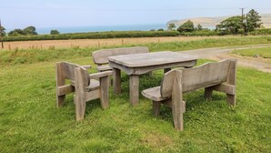 A rustic wooden table and benches set in a grassy field with a scenic view of the sea and hills in the background. - Ty Fferm (Newport)