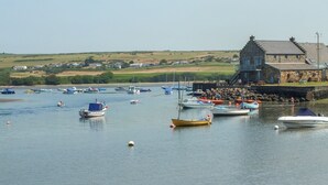 A harbor with various boats docked, a stone building with a staircase, and a grassy landscape in the background. - Ty Fferm (Newport)