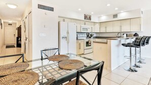 A modern kitchen with a central island, bar stools, and a dining area with a glass table and woven placemats.