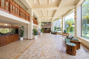 A spacious lobby with a large fish tank, potted plants, a reception desk, and a seating area with a view of the outdoors.