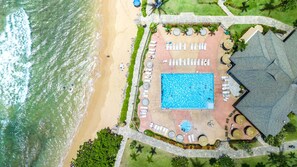 Vista aérea de un resort con piscina central, tumbonas y zona de playa.
