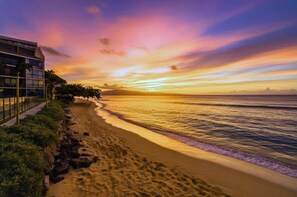 Une plage au coucher du soleil, un bâtiment doté d’un balcon et un ciel dégagé.