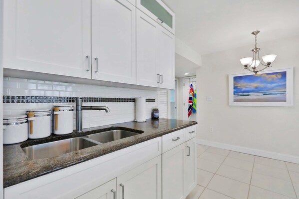 A kitchen with white cabinets, a granite countertop, a stainless steel sink, and a chandelier.