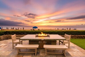 Une terrasse extérieure dotée d’un foyer, de sièges et offrant une vue sur la plage au coucher du soleil.