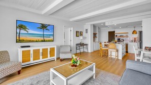 Un salon moderne avec un téléviseur à écran plat, un canapé, une table basse et un coin cuisine à l’arrière-plan.