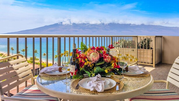 Une table dressée pour le dîner, avec vue sur l’océan et une montagne en arrière-plan.
