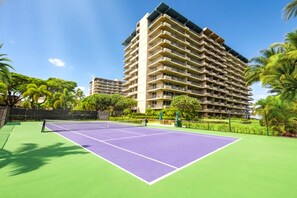 Ein Tennisplatz mit Netz, umgeben von einem Zaun und Palmen.