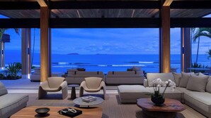 A modern living room with a view of the ocean, featuring a sofa, chairs, and a coffee table.