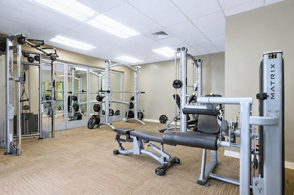 A gym with weightlifting equipment, mirrors, and a wooden floor.