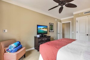 Una habitació d'hotel amb un llit, televisió, ventilador de sostre, escriptori i una cadira.