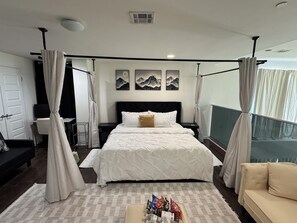 A hotel room with a four-poster bed, a desk, a chair, and a sofa.