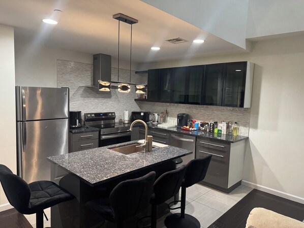 Una cocina moderna con una isla central, electrodomésticos de acero inoxidable y taburetes negros.