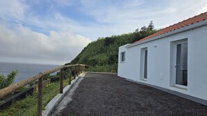 A white building with a red-tiled roof, a gravel path, and a view of the sea.