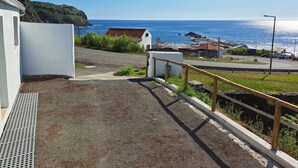 A coastal road with a white building, a small structure with a red roof, and a view of the sea.