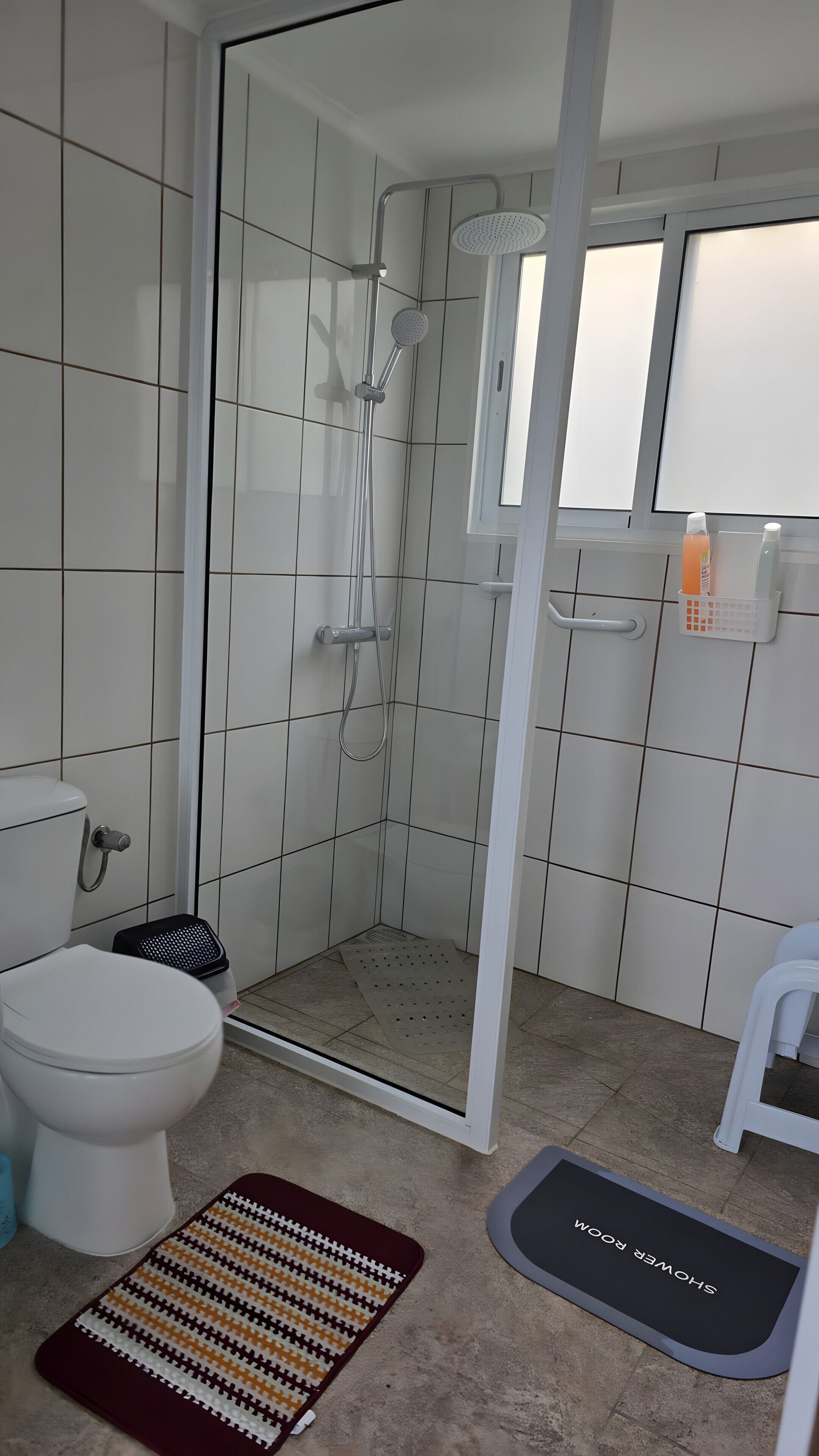 A bathroom with a glass-enclosed shower, a toilet, a bidet, and a small white stool.