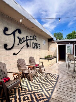 An outdoor seating area with Adirondack chairs, a patterned rug, and a wall with graffiti.