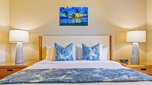 Une chambre d’hôtel avec un lit, deux lampes de chevet, un tableau représentant un coucher de soleil et une couvre-lit à motifs.