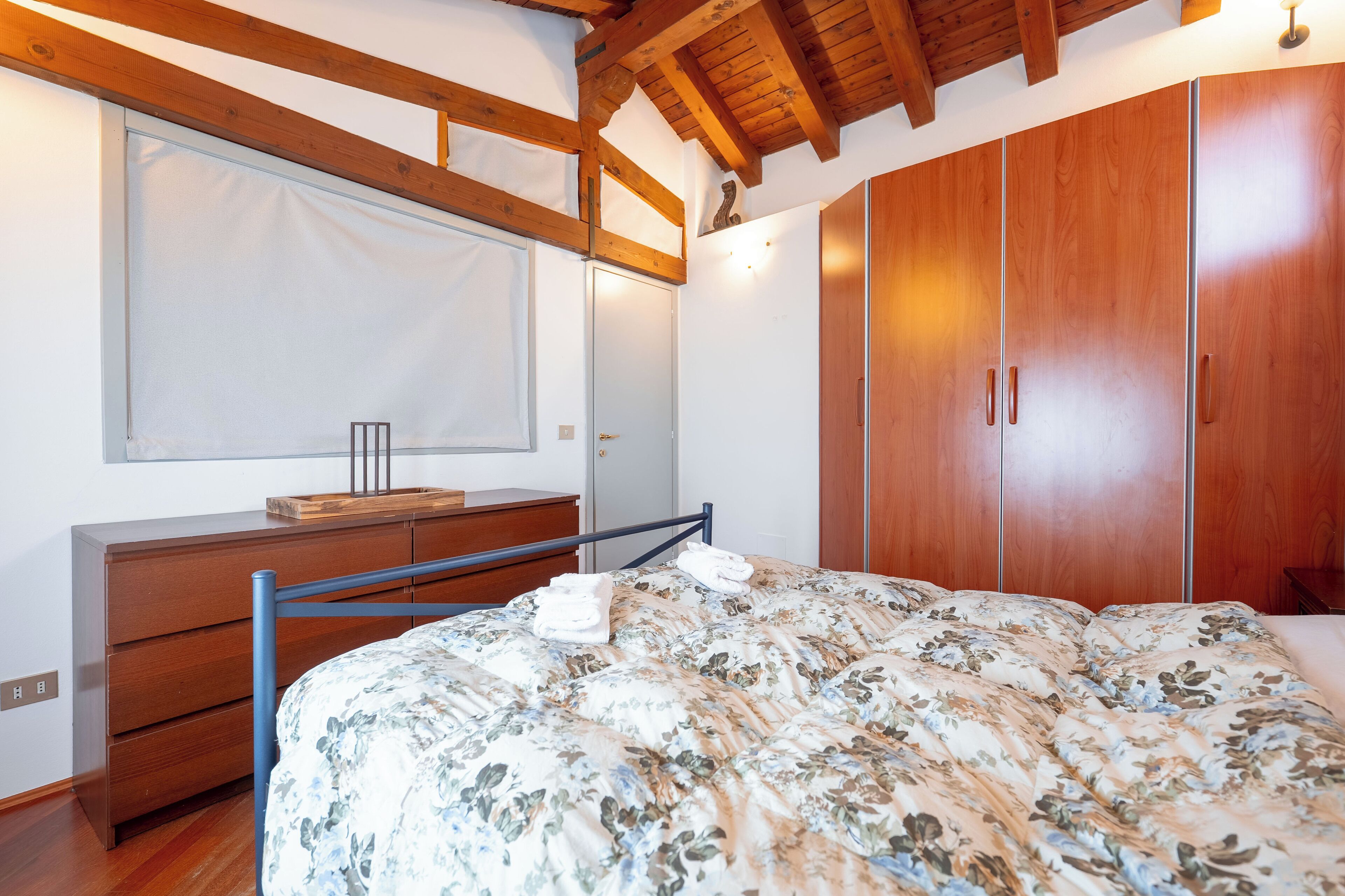 Una camera da letto con un'armadiatura in legno, un letto con copripiumino floreale, un comò in legno e una finestra con persiane.