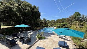A pool area with lounge chairs and umbrellas, surrounded by trees and a clear sky. - Countryside villa with swimming pool (Lambesc)