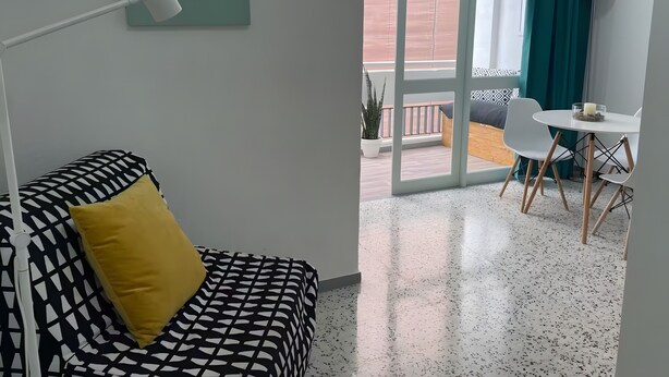 A modern room with a patterned sofa, a small table with a candle, and a balcony with a view. - Vacation Studio 'Puerto Centro House' with Balcony and Wi-Fi (Puerto de la Cruz)