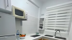 A compact kitchen with white cabinets, a microwave, a sink, and a window with blinds. - Vacation Studio 'Puerto Centro House' with Balcony and Wi-Fi (Puerto de la Cruz)