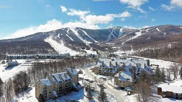 A snow-covered resort with multiple buildings, a ski slope, and mountains in the background.