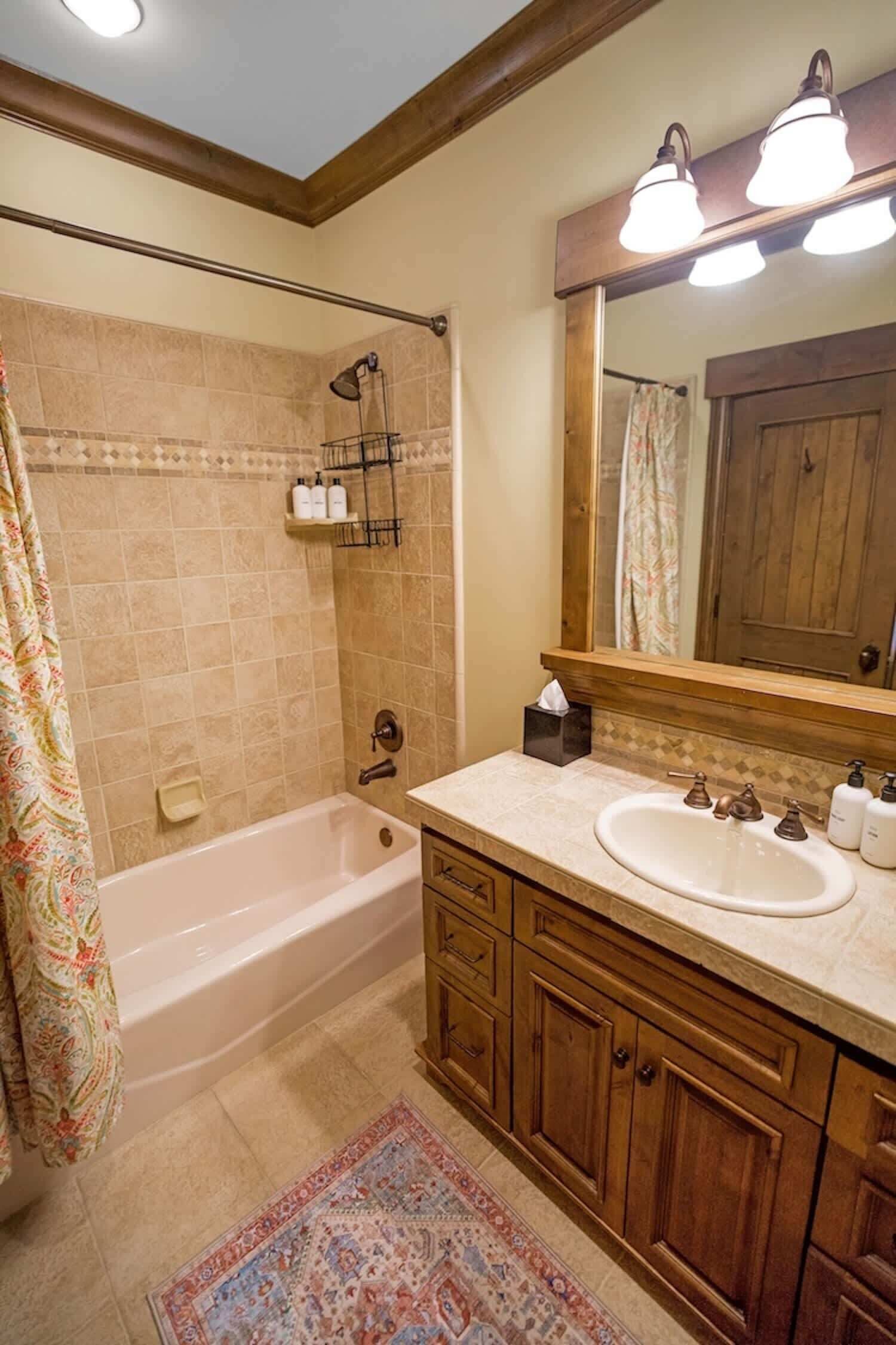 Une salle de bain avec une baignoire, un lavabo, des meubles en bois, un miroir et un rideau de douche.